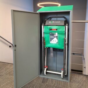 A grey Exitmaster Evacuation Chair Storage Cabinet with a transparent window or label area, designed to securely house an evacuation chair, against a white background.
